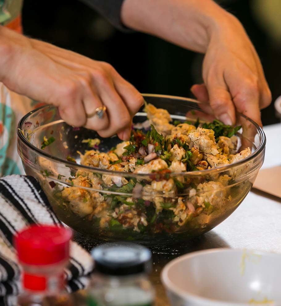 close up of hands mixing a glass bowl of chicken salad