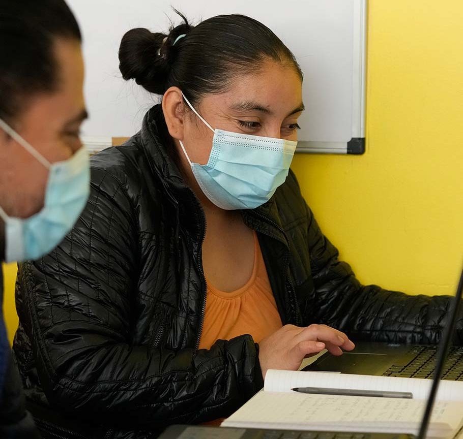 man and woman in disposable face masks look at laptop together