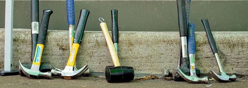 a collection of hammers and mallets resting against a curb