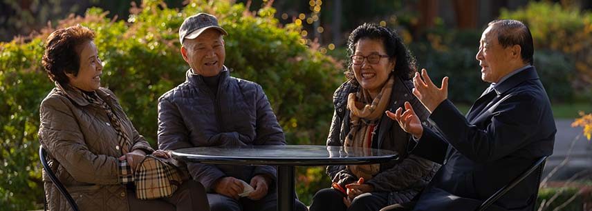 Asian American seniors sitting at an outdoor table laughing