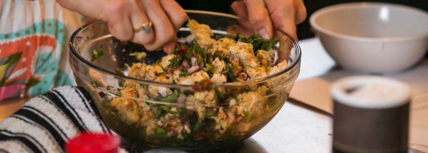 close up of hands mixing a glass bowl of chicken salad