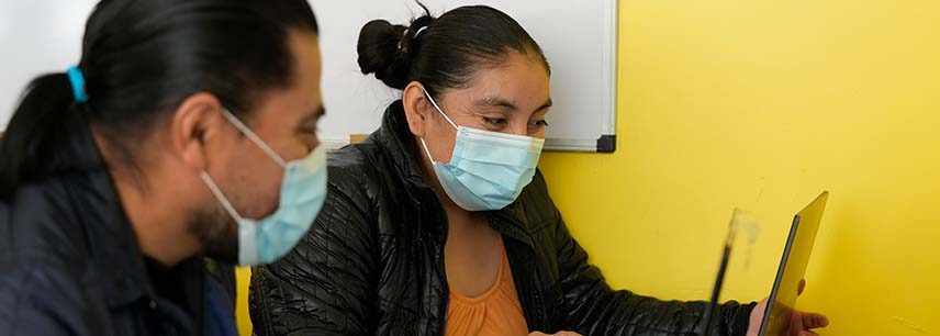 man and woman in disposable face masks look at laptop together